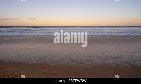 Mit Blick nach Osten über den Pazifik, Queensland, während die Sonne im Westen untergeht und darauf wartet, dass der Vollmond über dem Horizont aufgeht, während die Surfwellen Stockfoto