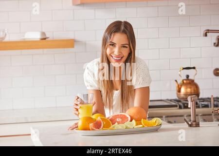 Porträt einer lächelnden Frau mit einem Glas frischen Zitrussaft in der Küche Stockfoto