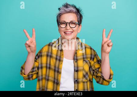 Porträt der fröhlichen netten Dame im höheren Alter, die V-Zeichen zeigt, Symbol Hi Kollegen Büroatmosphäre isolierter blaufarbener Hintergrund Stockfoto