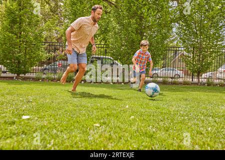 Vater und Sohn (8-9) spielen Fußball im Park Stockfoto