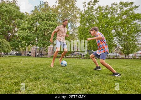 Vater und Sohn (8-9) spielen Fußball im Park Stockfoto