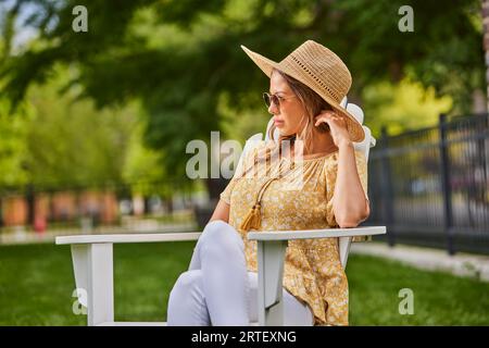 Frau mit Strohhut und Sonnenbrille, die sich im Park entspannt Stockfoto