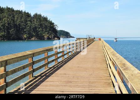 Blick auf einen langen Holzsteg am Horizont mit einer Gruppe von Kajakfahrern in der Nähe einer Insel auf der linken Seite und blauem Himmel über dem Himmel an einem sonnigen Tag Stockfoto