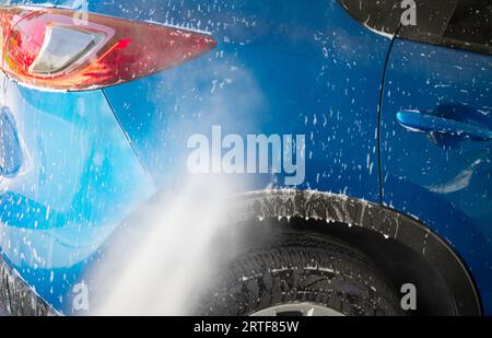 Autowäsche mit Hochdruckwasserspray. Reinigung des Autos. Servicekonzept Auto Care. Fahrzeugreinigung. Wasserspritzen auf ein Auto zur Reinigung von weißem Schaum Stockfoto