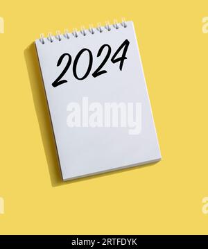 Neujahr 2024 auf Notizpapier auf hellgelbem Hintergrund geschrieben. Konzept in der Wirtschaft. Pläne für das neue Jahr. Lösungen, Pläne, Ziele, Maßnahmen, Überprüfung Stockfoto