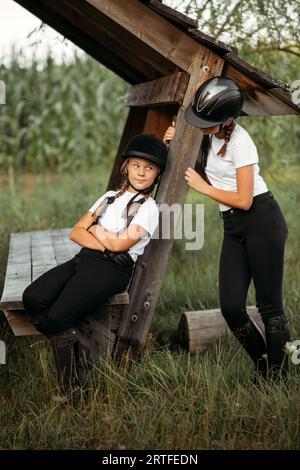 Porträt von Mädchen Jockeys, einer sitzt auf einer Bank, der zweite steht in der Nähe. Stockfoto