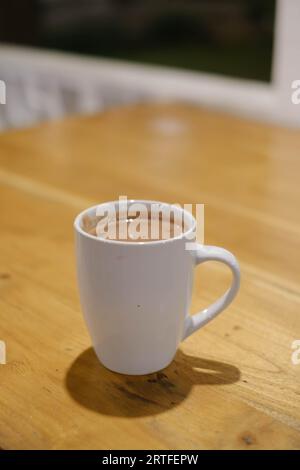 Porträt- oder vertikale und selektive Fokusaufnahme eines Kaffees in einem weißen Glas auf dem Holztisch Stockfoto