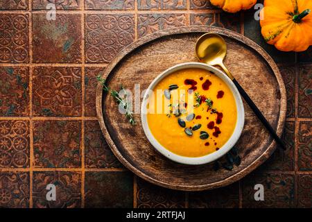 Kürbissuppe mit Kürbiskernen und Kürbiskernöl, serviert in einer Schüssel auf einem rustikalen Küchentisch Stockfoto