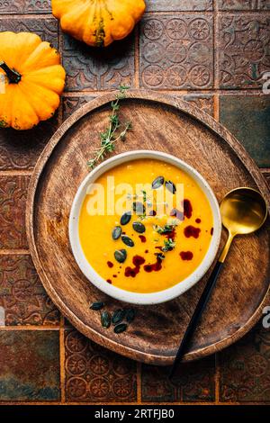 Kürbissuppe mit Kürbiskernen und Kürbiskernöl, serviert in einer Schüssel auf einem rustikalen Küchentisch Stockfoto
