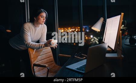 Eine durchdachte Geschäftsfrau arbeitet spät in der Nacht in ihrem Home Office und konzentriert sich auf ein digitales Marketingprojekt. Professionelle Frau, die mit einem Computer arbeitet Stockfoto