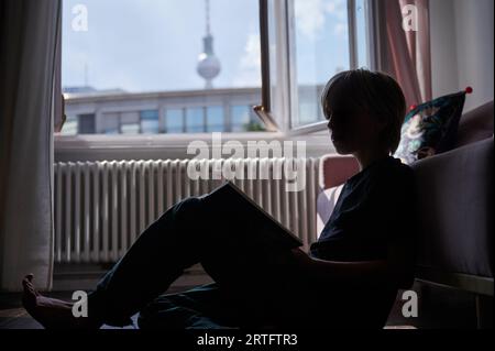 Berlin, Deutschland. 26. August 2023. Ein Kind liest, während es sich gegen eine Couch auf dem Boden lehnt. Annette Riedl/dpa/Alamy Live News Stockfoto