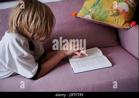 Berlin, Deutschland. 26. August 2023. Ein Kind liest, während es auf der Couch liegt. Annette Riedl/dpa/Alamy Live News Stockfoto