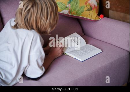 Berlin, Deutschland. 26. August 2023. Ein Kind liest, während es auf der Couch liegt. Annette Riedl/dpa/Alamy Live News Stockfoto