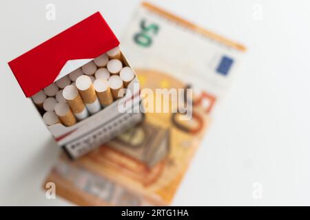 Euro-Geldscheine hundert und Zigarettenschachtel auf weißem Hintergrund. Konzepttabakupreise und Gesundheitskosten. Stockfoto