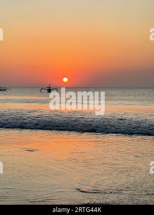 Ein einsames Schiff, das bei Sonnenuntergang in einem ruhigen Meer mit orangefarbenem Himmel schwimmt Stockfoto