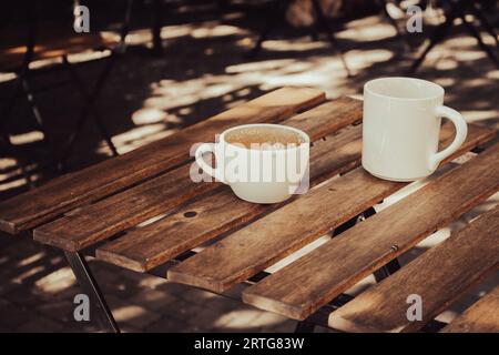 Zwei leere Kaffeetassen auf Holztisch. Frühstückstisch. Kaffeemöbel auf dem Bürgersteig. Getränke am Morgen. Cappuccino in weißen Tassen. Tägliche städtische Lebensweise. Stockfoto