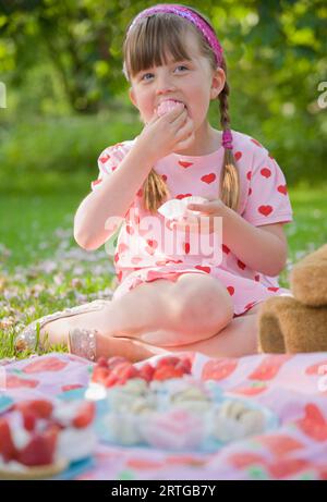 Junge Mädchen sitzt in einem Garten Lächeln auf den Lippen und einen kleinen Kuchen essen Stockfoto