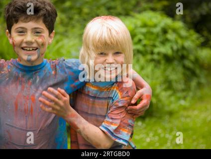 Zwei junge Jungs, die mit Aquarellfarbe bedeckt sind, lachen im Garten Stockfoto