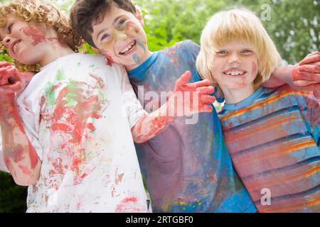 Junge, die mit Aquarellfarbe bedeckt sind, lachen im Garten Stockfoto