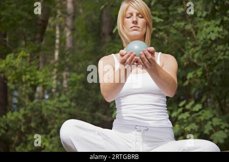 Junge Frau in der Meditation Schneidersitz sitzen durch einen Wald, eine Kugel in ihren Händen hält Stockfoto