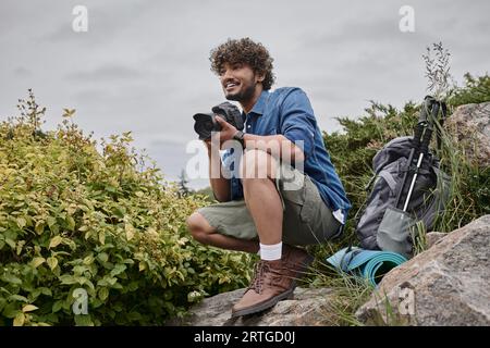 Reisefotograf Konzept, glücklicher indischer Mann, der ein Foto auf der Kamera an einem natürlichen Ort macht, Banner Stockfoto