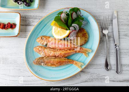 Köstlicher gegrillter Meerbarben-Fisch mit Beilagen wie Zitrone, Gemüse und Zwiebeln Stockfoto