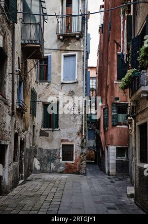 Gedämpftes rotes Wohngebäude mit grünen Fensterläden. Waschen hängt an der Schlange, die vom Fenster gestreckt ist, Venedig, Italien, mehrere Eingänge Stockfoto