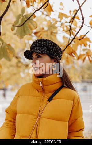 Schöne junge Dame in stilvolle warme Kleidung lächelnd und stehend Auf Baum an erstaunlichen Herbsttag auf der Stadtstraße Stockfoto