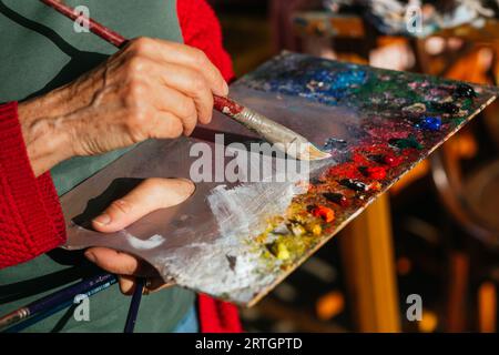 Von oben der Ernte unkenntlich ältere weibliche Malerin mischen Farben auf Farbpalette in der Kunstwerkstatt Stockfoto