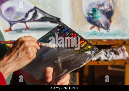 Von oben der Ernte unkenntlich ältere weibliche Malerin mischen Farben auf Farbpalette in der Kunstwerkstatt Stockfoto