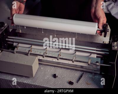 Von oben aus anonymer Buchbinder, der bei der Arbeit an der Werkbank in einer professionellen Werkstatt die Rolle mit Klebstoff in die Maschine einbringt Stockfoto