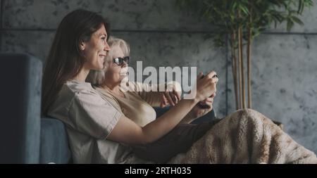 Glückliche schöne zwei aufgeregte lächelnde Frauen, die Videospiele spielen und das Gamepad in der Hand halten, auf dem Sofa sitzen und einen lustigen Wettbewerb haben. Verbringen Sie ein Wochenende Stockfoto