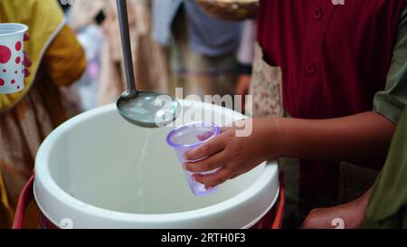 Gruppen von Menschen stehen an, um frische Getränke mit Plastikbechern zu nehmen. Stockfoto