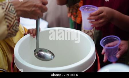 Gruppen von Menschen stehen an, um frische Getränke mit Plastikbechern zu nehmen. Stockfoto