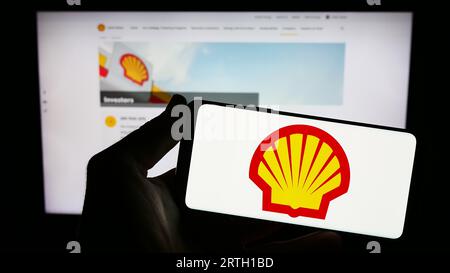 Person, die ein Mobiltelefon mit dem Logo des britischen Öl- und Gasunternehmens Shell plc auf dem Bildschirm vor der Geschäftswebseite hält. Konzentrieren Sie sich auf das Display des Telefons. Stockfoto