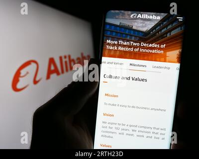 Person, die ein Mobiltelefon mit der Website des chinesischen Unternehmens Alibaba Group Holding Limited auf dem Bildschirm mit Logo hält. Konzentrieren Sie sich auf die Mitte der Telefonanzeige. Stockfoto