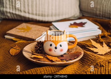 Gemütliches Herbsthaus. Herbstgemütlicher Lesebereich mit einer Decke, Kerzen, Herbstlaub, Tasse Kaffee auf braunem Bett im Hintergrund zu Hause. Kalte Jahreszeit Stockfoto
