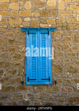 Blau lackiertes Holzfenster an der Wand aus gelbem Stein, dekoratives architektonisches Steinhaus Beispiel. Hochwertige Fotos Stockfoto