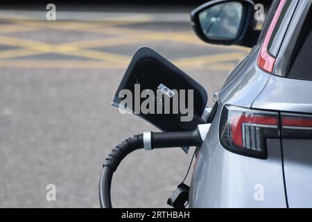 Eine Ladebuchse und ein Kabel eines Elektrofahrzeugs, das an einer Autobahndienststelle in Exeter Großbritannien aufgeladen wird Stockfoto