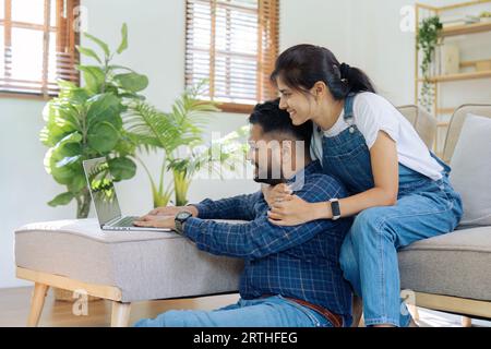 Glückliche liebende Familie indisches Paar umarmt sich auf Couch zu Hause und konzentriert sich auf Laptop-Bildschirm Stockfoto