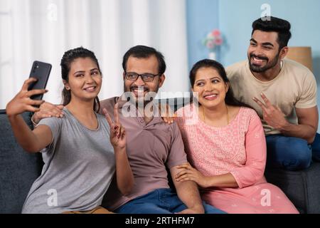 Fröhliche indische Eltern mittleren Alters mit Geschwistern, die Selfie auf dem Handy zu Hause nehmen - Konzept von Familienzusammengehörigkeit, Technologie-Wiedersehen und glücklich Stockfoto