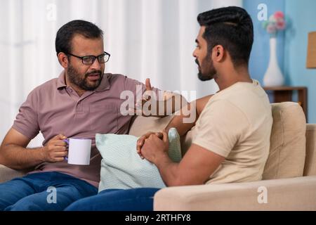 Seriöser indischer Vater, der mit seinem Sohn diskutiert, während er zu Hause Kaffee trinkt - Konzept von elterlicher Beratung, Familienbetreuung und Teilhabe am Leben Stockfoto