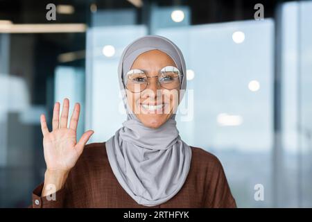Porträt einer jungen muslimischen Frau in einem Hijab, die im Büro sitzt und vor der Kamera lächelt. Stockfoto