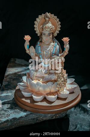 Hindu-Kosmos Maha laxshmi Statue mit Blumengirlande auf schwarzem Hintergrund verziert. Statue der Göttin des Reichtums, Kopierraum, selektiver Fokus. Stockfoto