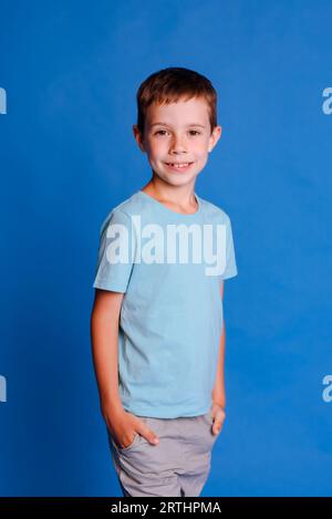 Fröhlicher lächelnder Junge im blauen Mockup-T-Shirt mit Blick auf die Kamera über hellblauem Studiohintergrund Stockfoto
