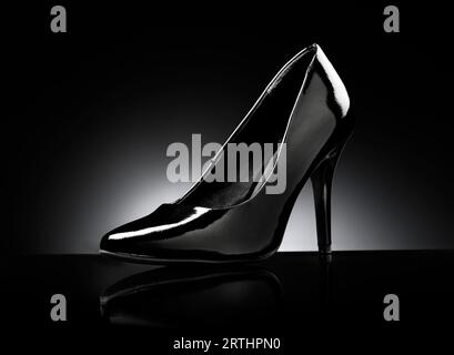 Schwarz glänzender Stiletto-Pumps für Damen auf schwarzem reflektierendem Hintergrund Stockfoto