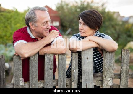 Ein älteres Paar, das in der Nähe eines Holzzauns im Garten steht Stockfoto
