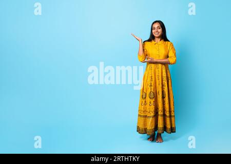 Indische Dame In Traditionellem Gelben Kleid Zeigt Copy Space, Studio Stockfoto