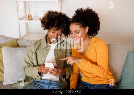 Black Ehefrau zeigt auf Screen, wenn das Paar das Smartphone Indoor benutzt Stockfoto