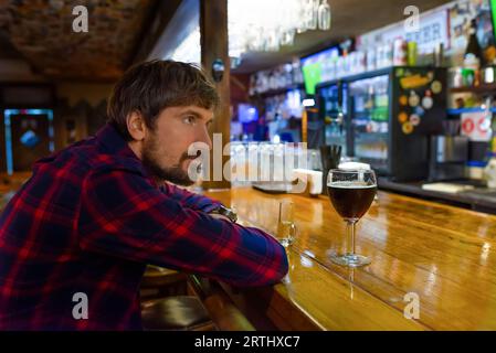 Ein Mann sitzt alleine an der Bar und trinkt Alkohol. Trauriger depressiver Betrunkener, der unter Alkoholmissbrauch leidet Stockfoto
